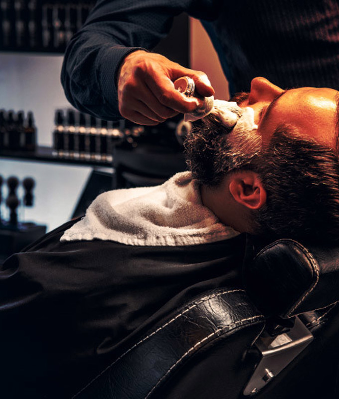 Barber applies shaving foam to a man's face in a saloon.